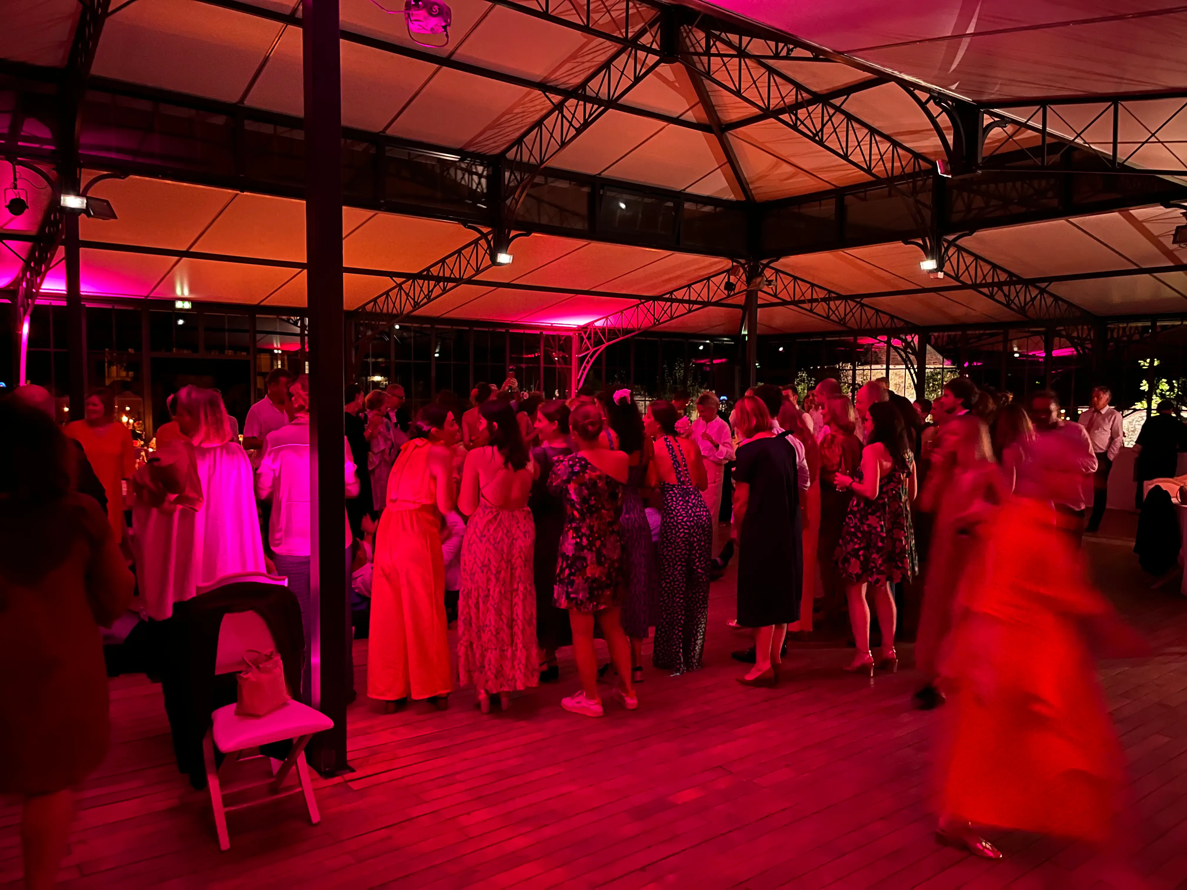 Invités sur la piste de danse d'un mariage, sous une verrière éclairée de lumières roses et rouges