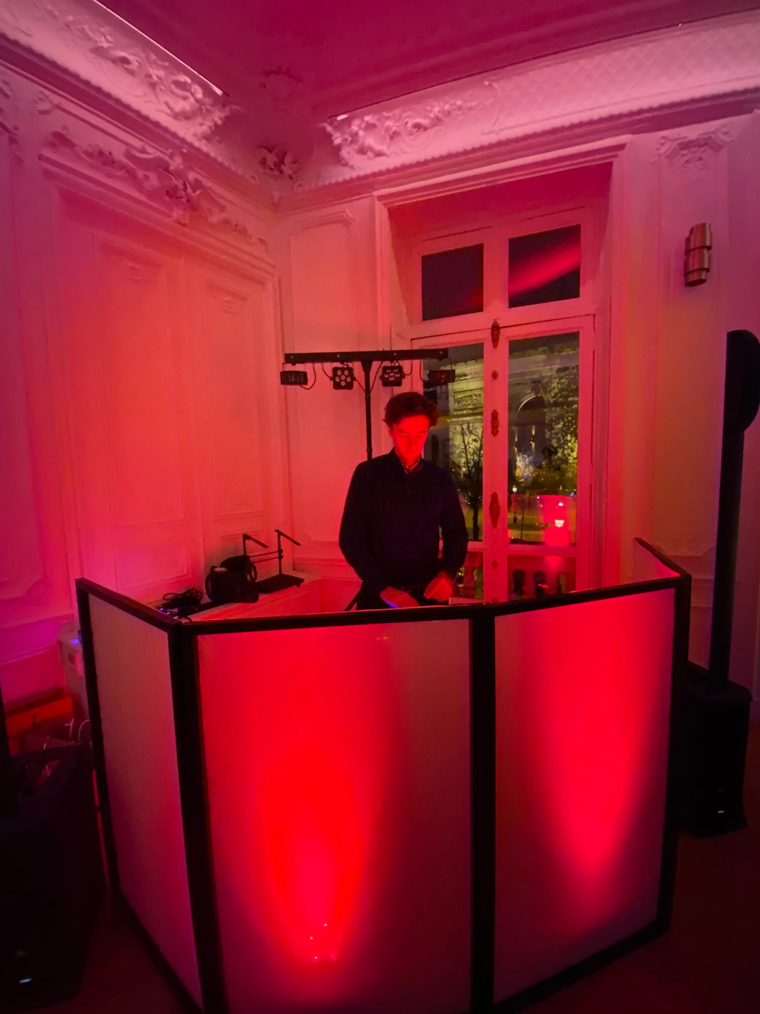 Cabine DJ éclairée en rouge dans un salon à moulures, pendant une soirée privée près de l'Arc de Triomphe